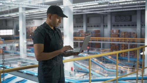 Logistics Transportation Warehouse Facility: Associate Worker Using Laptop in Retail Distrubution Center, Monitoring the Conveyors Loading Online Ordered Product Boxes for Delivery to Customers photo