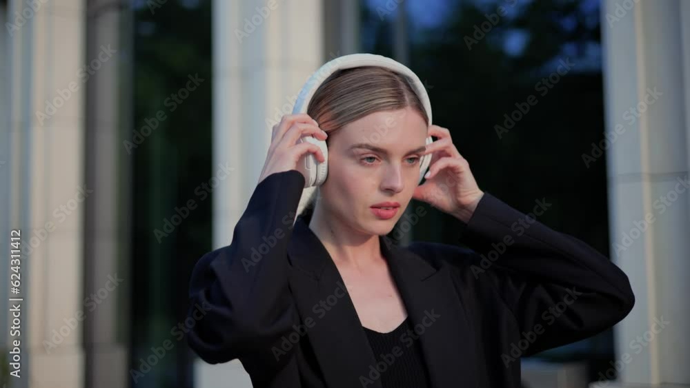 Attractive young caucasian woman putting headphones and enjoying music on the urban city, Female listening to music, song, podcast, or audiobook looking at camera with friendly smile outdoor. Attractive young caucasian woman putting headphones and enjoying music on the urban city, Female listening to music, song, podcast, or audiobook looking at camera with friendly smile outdoor.