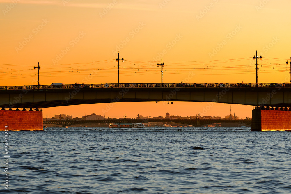 Reinforced concrete bridge over the big river of the old city at sunset, side view. Span of a drawbridge in a blood orange evening.