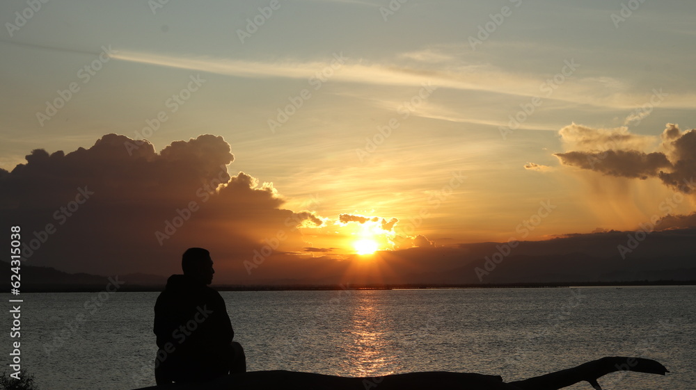 Fototapeta premium Silhouette of a man sitting on the lake and watching the sunset