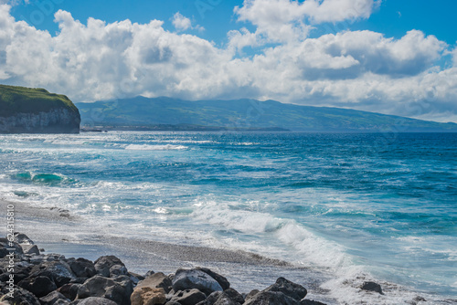 Waves and turquoise water breaking on the black sand of Santa Bárbara beach with cloudy mountain in the background, São Miguel - Azores PORTUGAL