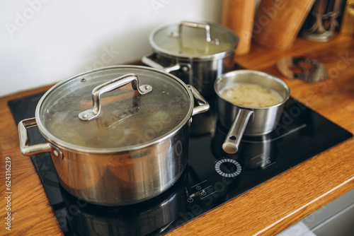 Cooking pots with tasty soup on electric stove in kitchen at the home, food concept