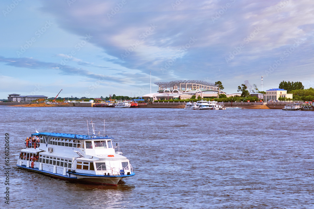 A white motor ship floats down the river on a sunny summer evening. Embankment in the background. A white motor ship floats down the river on a sunny summer evening. Embankment in the background.