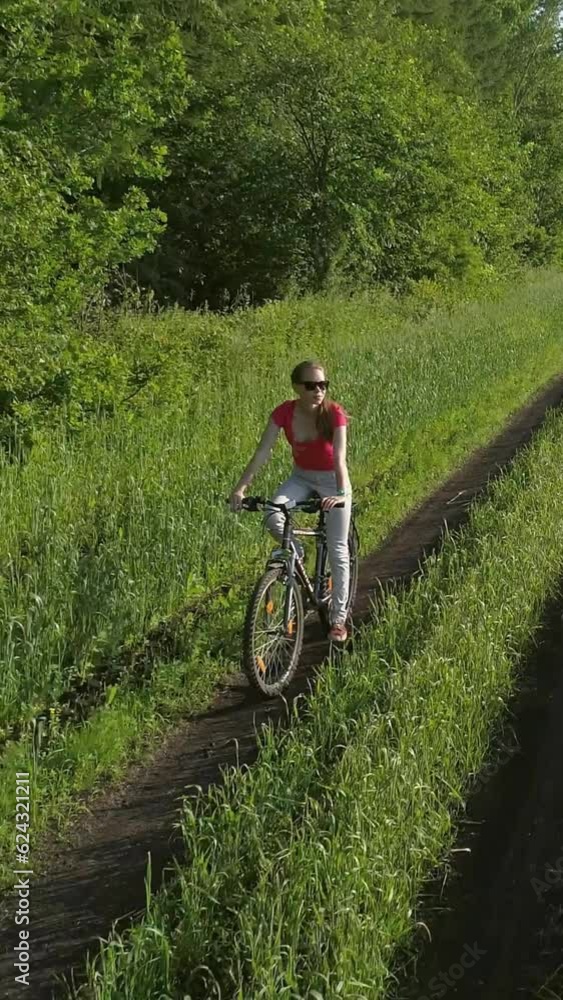 Cute young girl on bicycle in green field at summer, drone shooting. Vertical video Cute young girl on bicycle in green field at summer, drone shooting. Vertical video