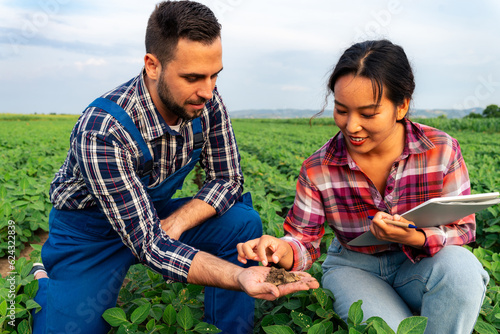 A Chinese woman and a Caucasian man, agronomists in a soybean field, examining soil conditions for optimal growth.