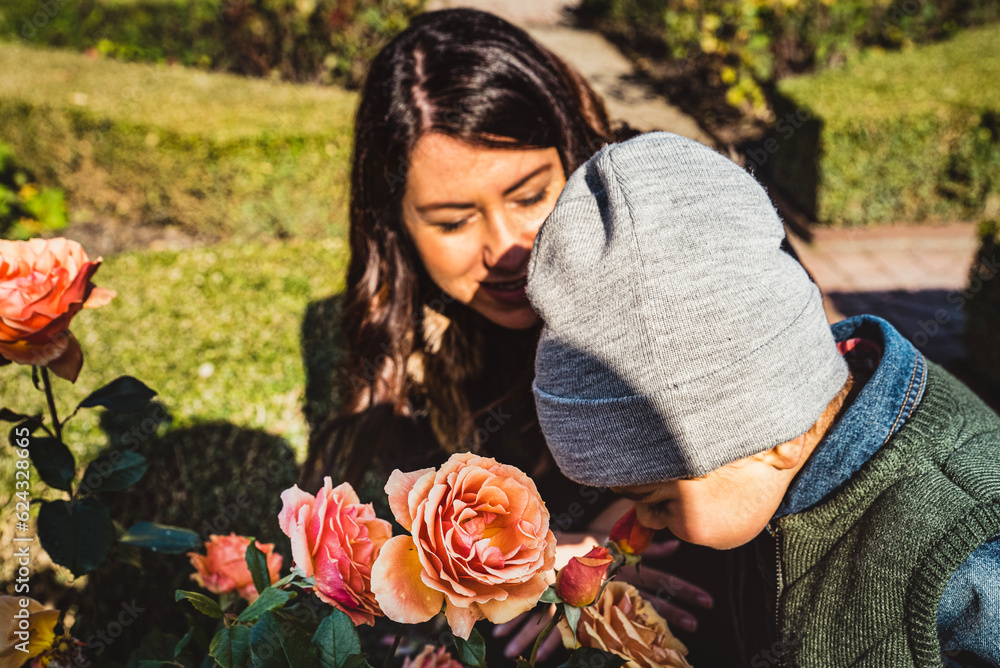 A small kid smelling the delicate fragrance of a rose with his mom