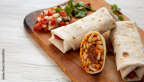 Homemade chorizo breakfast burritos on a rustic wooden board on a white wooden surface, low angle view. Close-up.