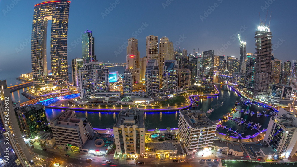 Fototapeta premium Panoramic view of Dubai Marina with several boat and yachts parked in harbor and skyscrapers around canal aerial day to night timelapse.