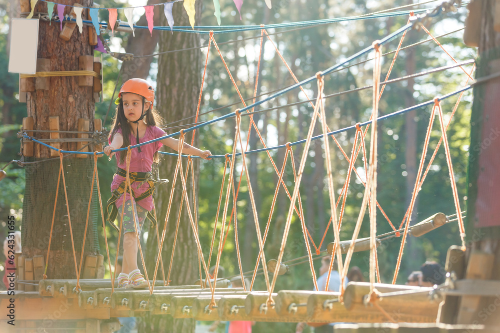 Little brave caucasian girl treerunner fasten the carabiner clip before climbing at outdoor treetop climbing adventure park