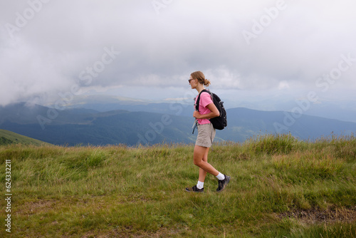 Girl is watching on mountains view. Woman is hiking in mountains in summer.Beautiful mountain landscape in Carpathians, Romania.Travel and tourism.Woman hiker is enjoying the mountain view.