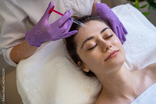 Top view of a woman receiving rejuvenation injection in face, anti aging non surgical cosmetic procedure in beauty salon. Beautician specialist hands in gloves photo