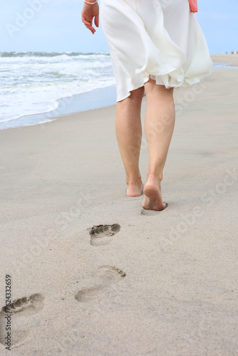 Beach trip - a woman walks along a sandy beach in a relaxed way, leaving footprints in the sand. Close-up of women's feet and shins on golden sand.