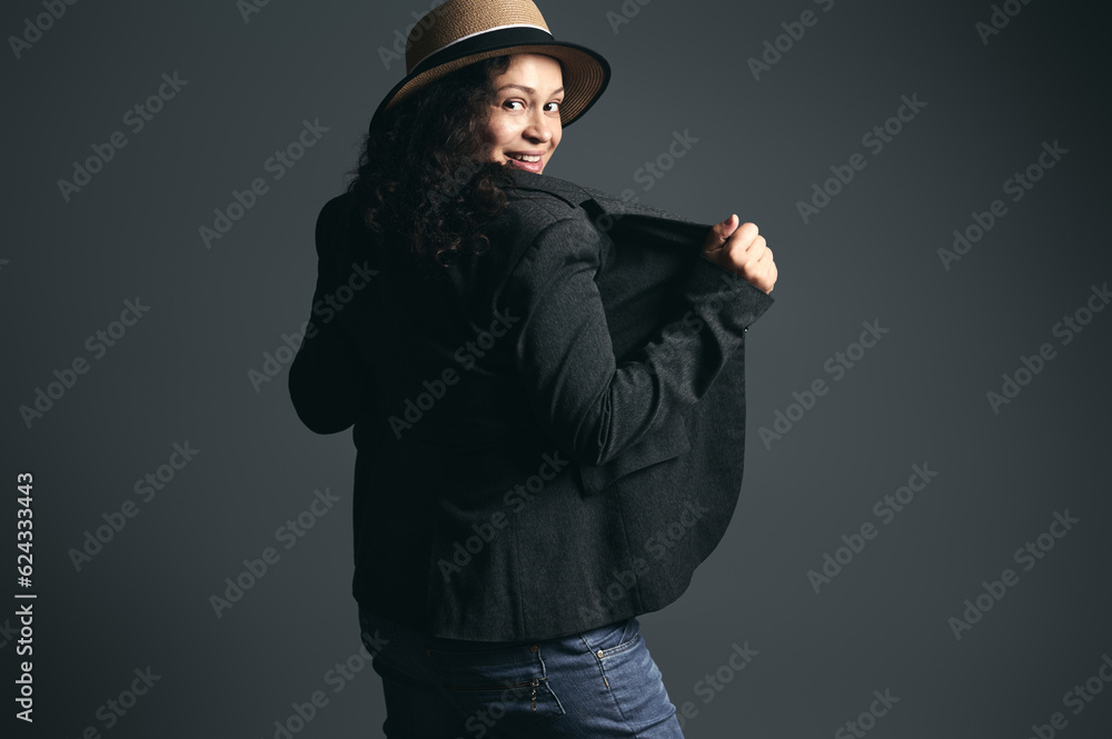 Fashionable curly Latina woman in straw hat and stylish blazer, looking through her shoulders, posing back to camera Fashionable curly Latina woman in straw hat and stylish blazer, looking through her shoulders, posing back to camera