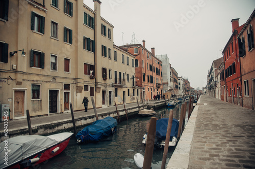 A serene Venice canal with boats tied to posts  lined by charming sidewalks on each side.