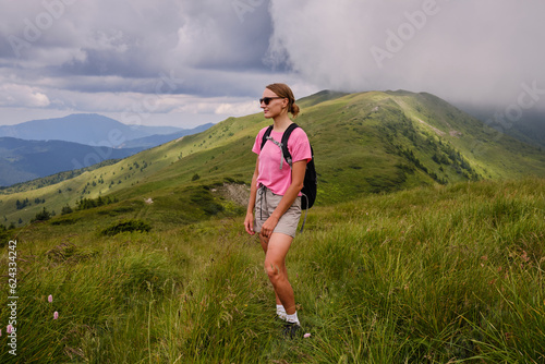 Girl is watching on mountains view. Woman is hiking in mountains in summer.Beautiful mountain landscape in Carpathians, Romania.Travel and tourism.Woman hiker is enjoying the mountain view.