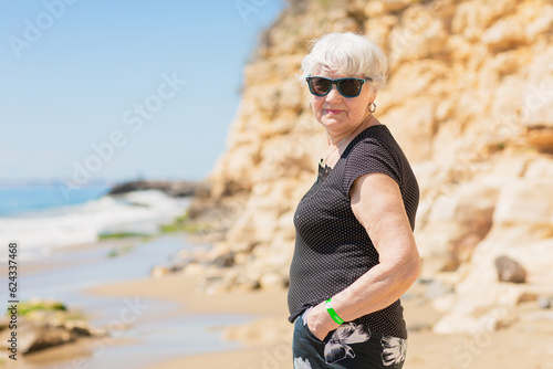 Senior woman of retirement age in sunglasses standing on the shore  looking at the sea and enjoying