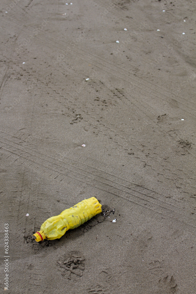 An old, yellow bottle discarded on the beach sand with tire tracks on it, causing environmental pollution. An old, yellow bottle discarded on the beach sand with tire tracks on it, causing environmental pollution.