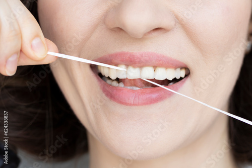Woman brushing her teeth with dental tape close-up. Small distance between teeth