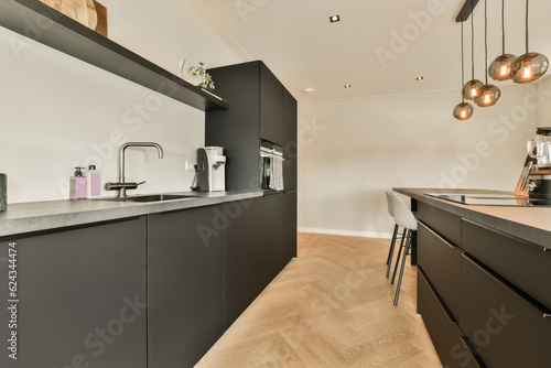 a modern kitchen with wood flooring and black cabinetry in the room is lit by pendants hanging on the ceiling