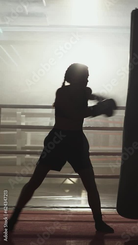 Kickboxing, woman fighter trains his punches, beats a punching bag, training day in the boxing gym, strength fit body, the girl strikes fast, vertical video.