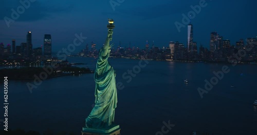 Aerial Helicopter Cinematic View of the Statue of Liberty with Manhattan Skyline Cityscape in the Evening. Panoramic View of New York City Skyscrapers and Jersey City Buildings at Sunset