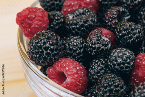 Close-up of glass bowl with red and black raspberries. Macro shot.