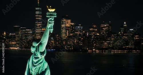 Cinematic Helicopter Pass by the Statue of Liberty at Night. Close Up Panoramic Aerial Footage of the Illuminated Roman Goddess Holding a Torch. Landmark New York Monument with Manhattan Skyscrapers