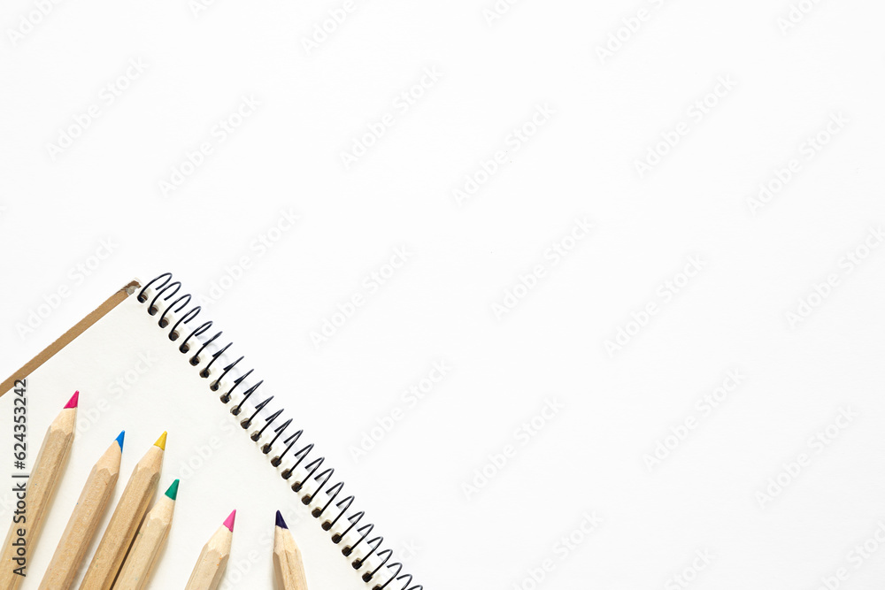 Fototapeta premium Wooden pencils of different colors and a notebook on a white background.