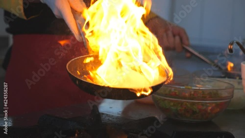 Detail view on flaming skillets in hand of professional chef. Male cook tossing and frying vegetables cooking tasty flambe style dish for visitors of restaurant. Concept of cooking. Slow mo Side view