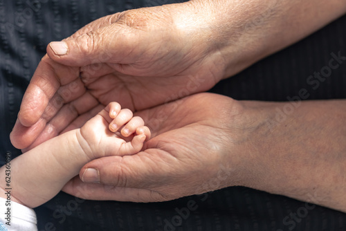 The handle of a newborn in the hands of a grandmother, close-up.