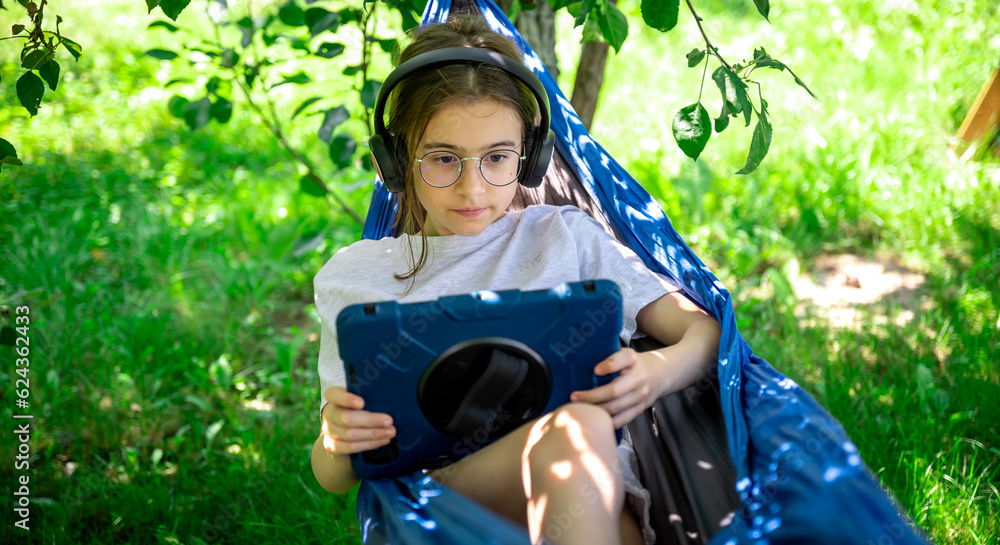 Girl with a tablet in a hammock in the garden.