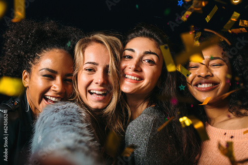 Four happy women taking selfie under golden confetti at night