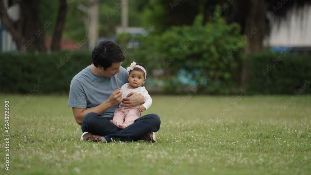 father talking and playing with his infant baby while sitting on a grass field father talking and playing with his infant baby while sitting on a grass field