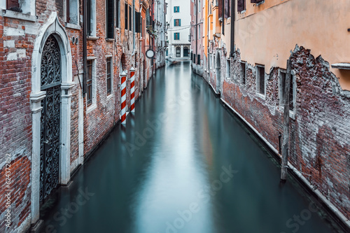 Narrow water canal and red brick worn out buidings built on water in Venice, Italy. Long exposure photography.