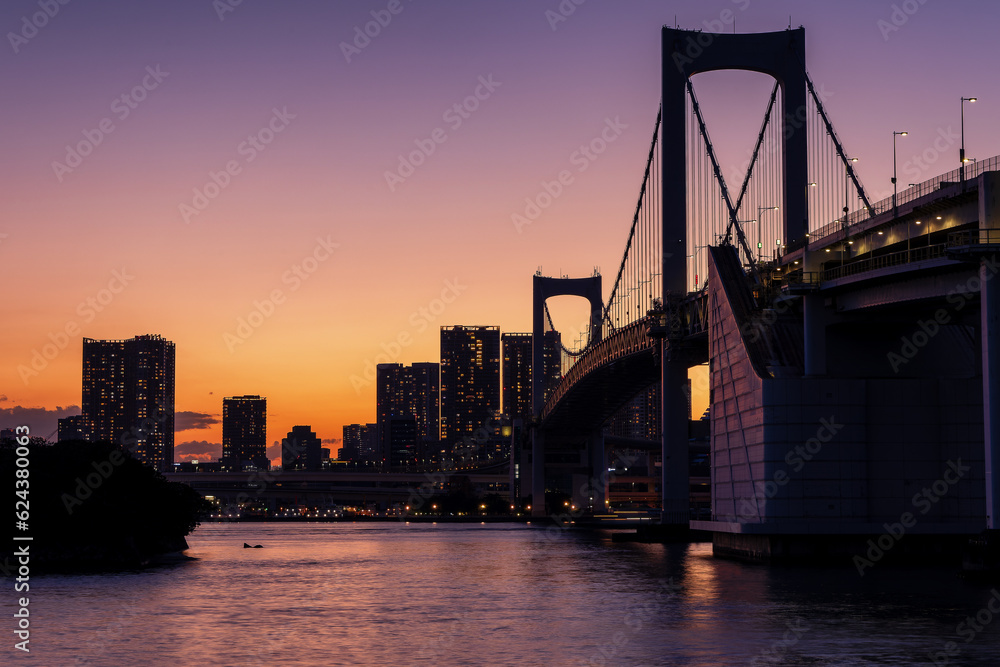 Purple and orange sky during sunset behind the skyscrapers of Tokyo and the Rainbow Bridge in Tokyo Bay