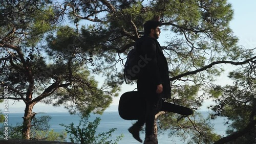 a musician with a guitar in a case walks in nature. handsome brunet