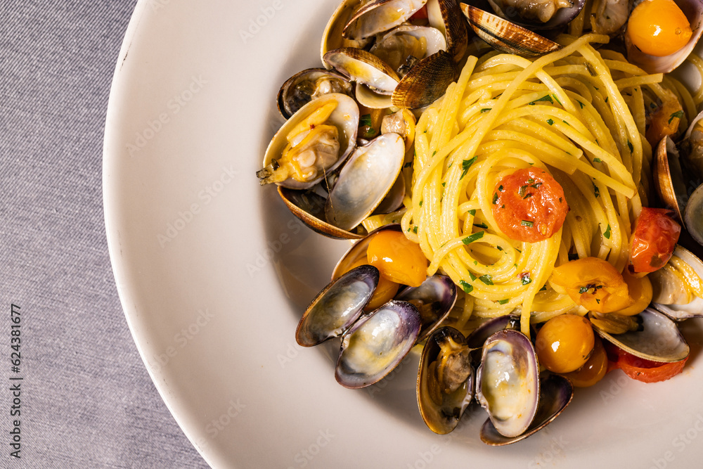 Piatto di spaghetti con sugo di vongole veraci, pomodori gialli e prezzemolo servito come primo piatto in un ristorante elegante Piatto di spaghetti con sugo di vongole veraci, pomodori gialli e prezzemolo servito come primo piatto in un ristorante elegante