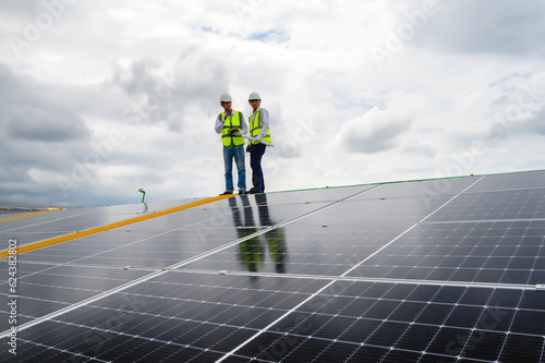 Young Engineers and Specialist Technicians Discuss and Check Quality of Installing Solar Photovoltaic Panels and Use App Technology Checking Accumulated power generation from Solar Panel on Tablet.