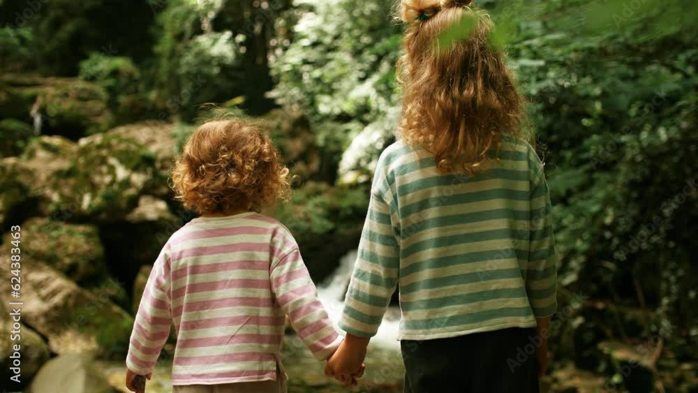 Two little sisters look at beautiful waterfall in the woods Two little sisters look at beautiful waterfall in the woods