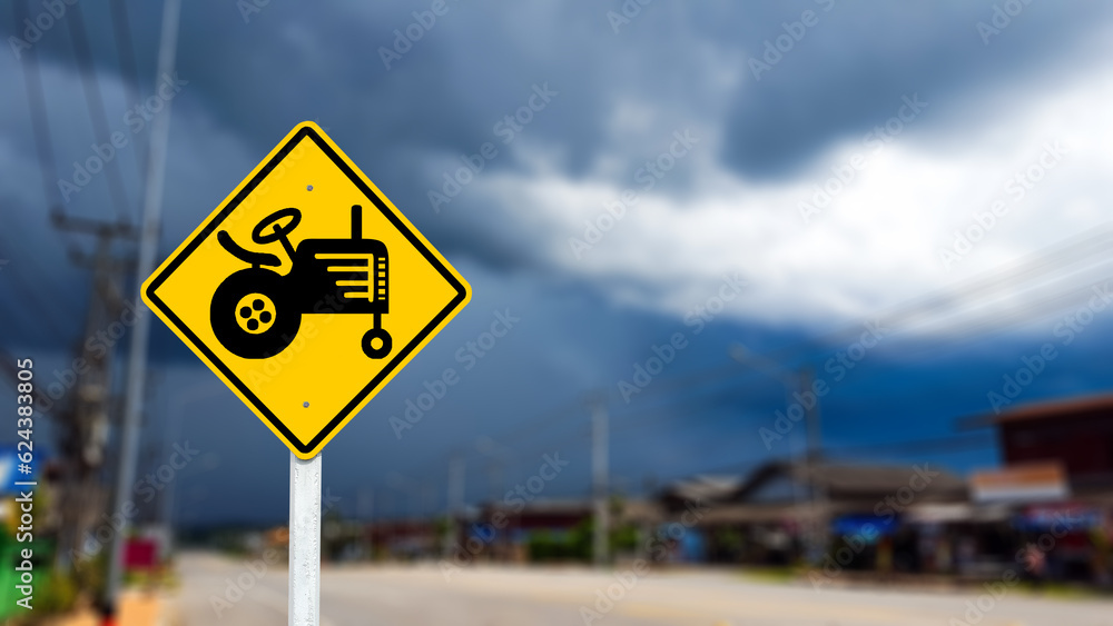Graphic of tractor on yellow sign on blurred background to warn traffic to aware of agricultural vehicles crossing the street