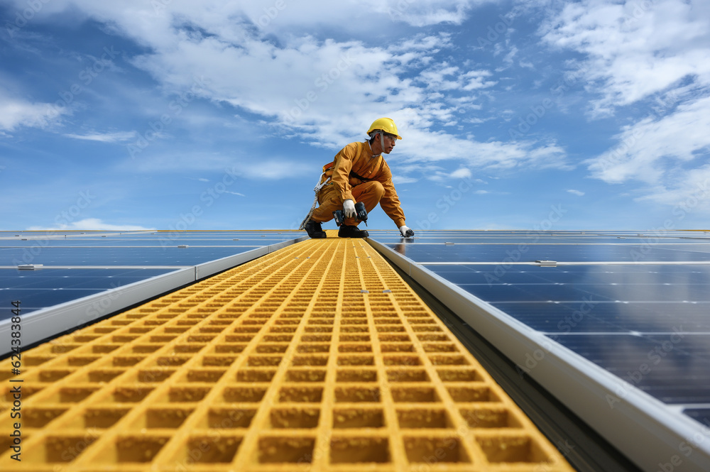 Technician Young Wearing Safety Protective Clothing with Installing Tool while Install Solar Panel or Photovoltaic in Daytime on Factory Roof Buildings.