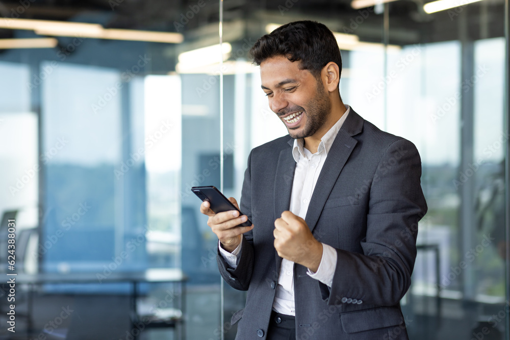 Young arab businessman happy celebrating victory reading news online, man got win holding joyfully hand up triumph gesture. Young arab businessman happy celebrating victory reading news online, man got win holding joyfully hand up triumph gesture.