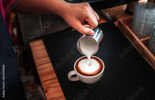 Barista hand pouring milk into coffee making a cappuccino. Professional barista preparing coffee on the counter.