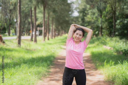 Asian woman wearing pink gym clothes Camlang warm up and stretch before running at the park.