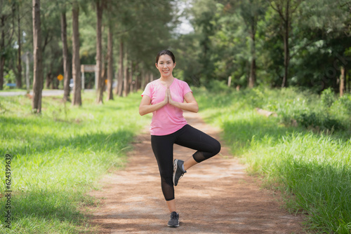 Asian woman in pink sportswear doing yoga in a park full of natural plants.