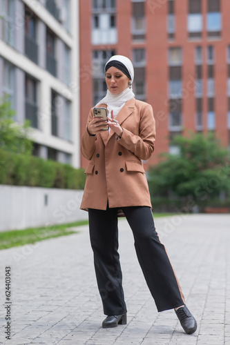 Young woman in hijab using smartphone outdoors.  © Михаил Решетников
