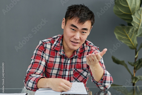 Принти на полотні Young Asian man sitting at the table with his chin propped