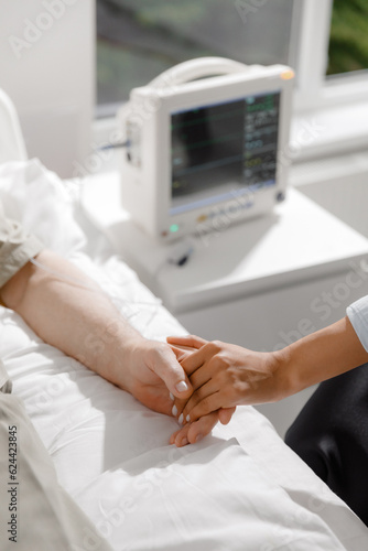 In the hospital room old man patient laying on the hospital couch while one family member holding his hands closeup to the camera capturing video