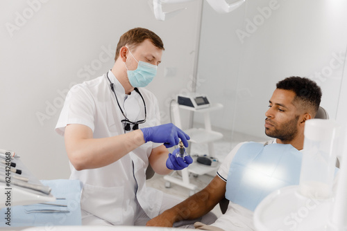 In a modern dental clinic the dentist with protective mask explains on the tooth model to the patient how the braces looking on tooth the patient sitting down on the dentist chair