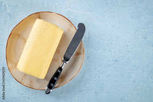 A block of butter with a knife on a plate, overhead flat lay shot on a light slate background, with copy space photo
